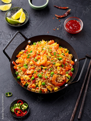 Stir fry rice with vegetables and shrimps in black iron pan. Slate background. Close up.
