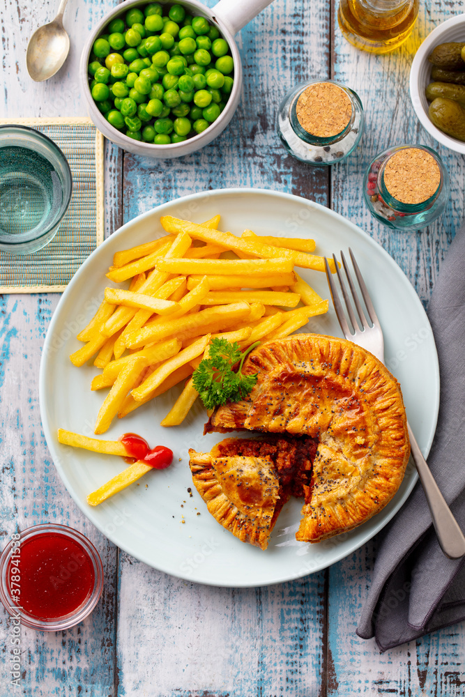 Meat pie with french fries on a white plate. Wooden background. Top view. Meat pie with french fries on a white plate. Wooden background. Top view.