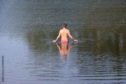 Man walks out into the lake for a swim with reflections on calm water