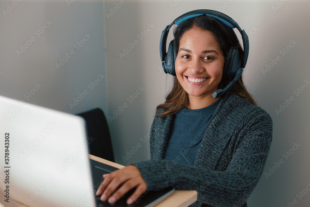 Young woman working on laptop at standing desk with earphones Young woman working on laptop at standing desk with earphones