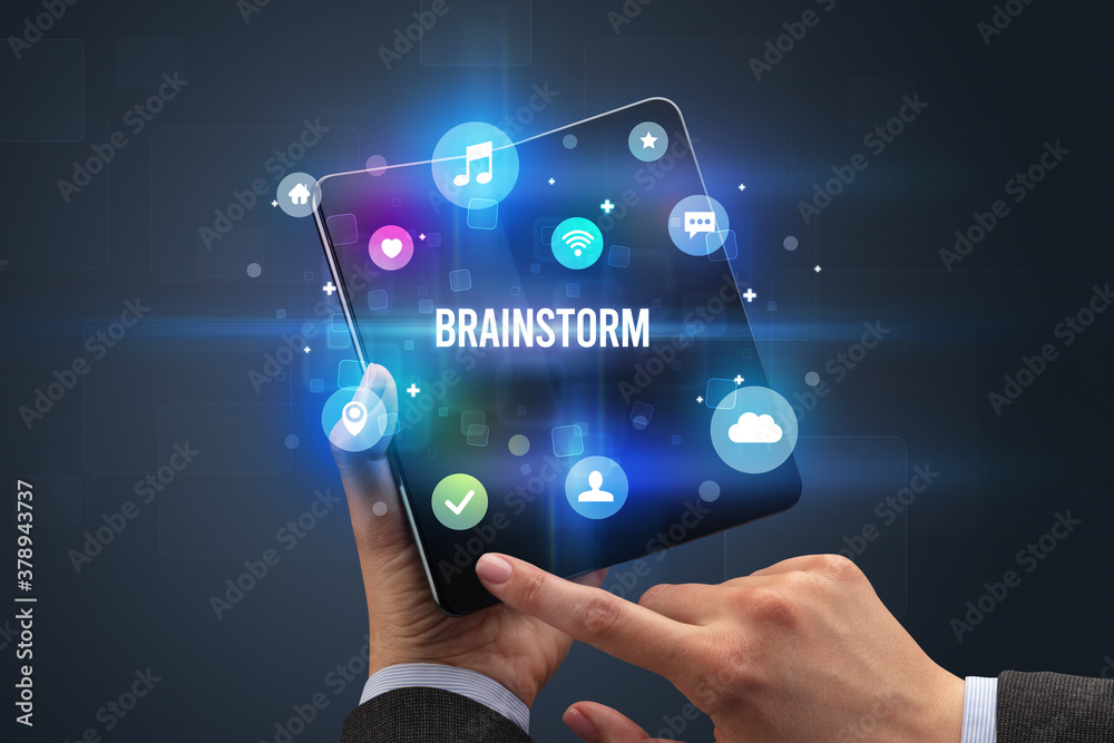 Naklejka premium Businessman holding a foldable smartphone with BRAINSTORM inscription, social media concept