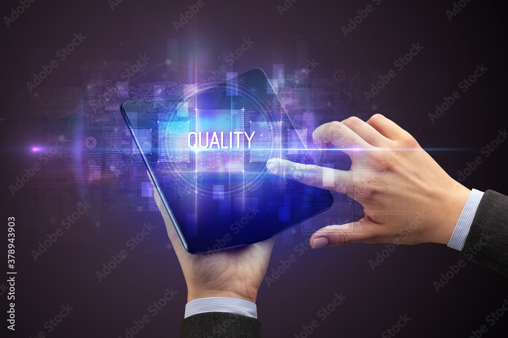 Obraz premium Businessman holding a foldable smartphone with QUALITY inscription, new technology concept