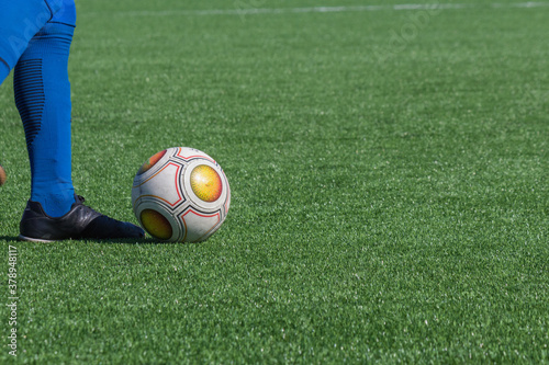 Close-up of foot of a soccer player in blue golf or leggings next to a soccer ball on a green football field