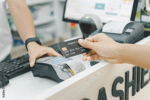 A hand of a customer is paying by contactless credit card with NFC technology. A seller with a credit card reader machine at the counter.  A female customer is holding a credit card. Focus on hand.