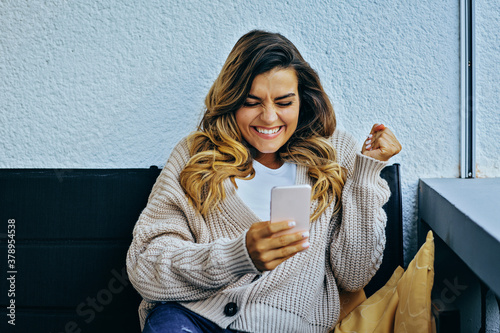 Young excited woman reacting  to news on phone, holding fist celebrating success, having great time photo