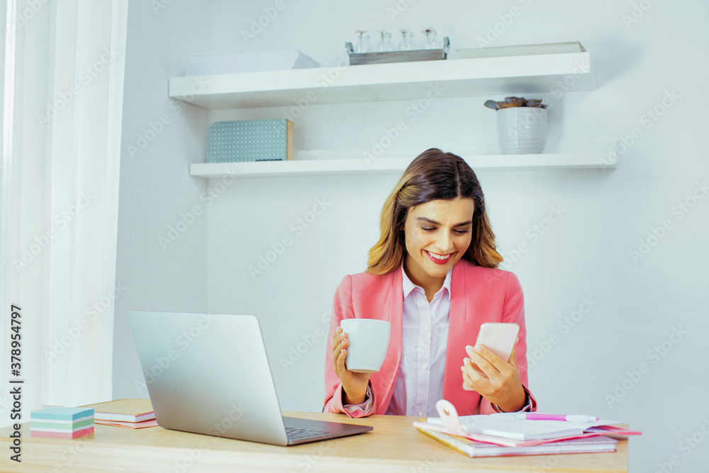 Young happy woman in pink business jacket working from home, holding phone and coffee Young happy woman in pink business jacket working from home, holding phone and coffee