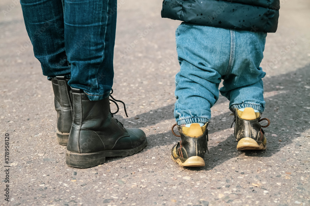 Teaching the baby to walk. An adult leads a child 1 year on the asphalt in the Park. Mother teaches her daughter 1 year. Teaching the baby to walk. An adult leads a child 1 year on the asphalt in the Park. Mother teaches her daughter 1 year.