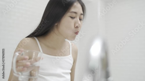 A cute Asian woman brushing her teeth and gargling in front of the mirror after waking up every morning.
