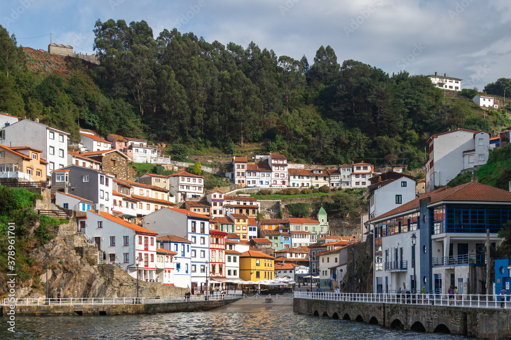 Traditional fishing village pictured from the sea. Natural harbor between the hills of the coastline. White houses with orange roofs. Colorful buildings. Cudillero, Asturias, North of Spain