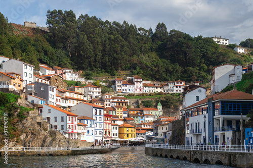 Traditional fishing village pictured from the sea. Natural harbor between the hills of the coastline. White houses with orange roofs. Colorful buildings. Cudillero, Asturias, North of Spain © Alba