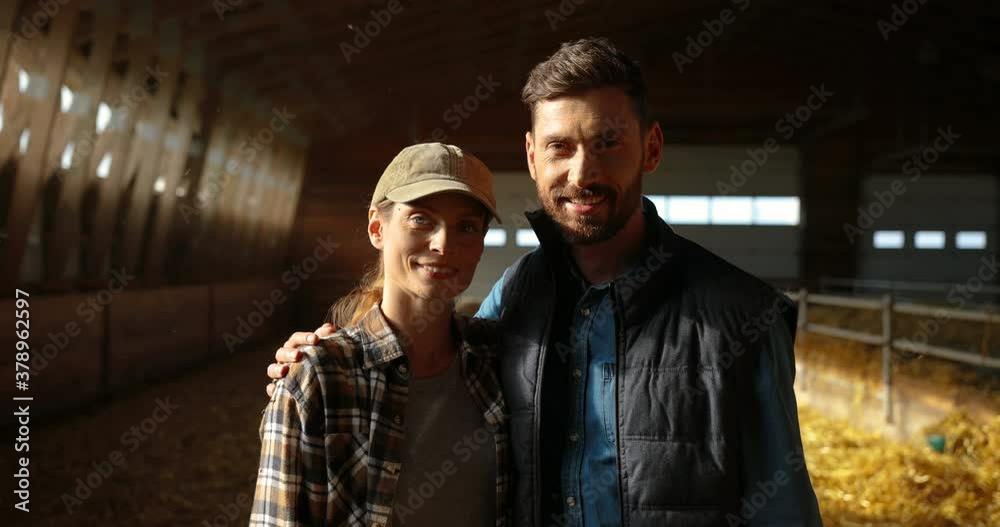 Portrait of handsome Caucasian man and beautiful woman standing in stable with flock of sheep on background, looking at each other and hugging. Shepherds smiling in hugs. Farming concept. In shades. Portrait of handsome Caucasian man and beautiful woman standing in stable with flock of sheep on background, looking at each other and hugging. Shepherds smiling in hugs. Farming concept. In shades.