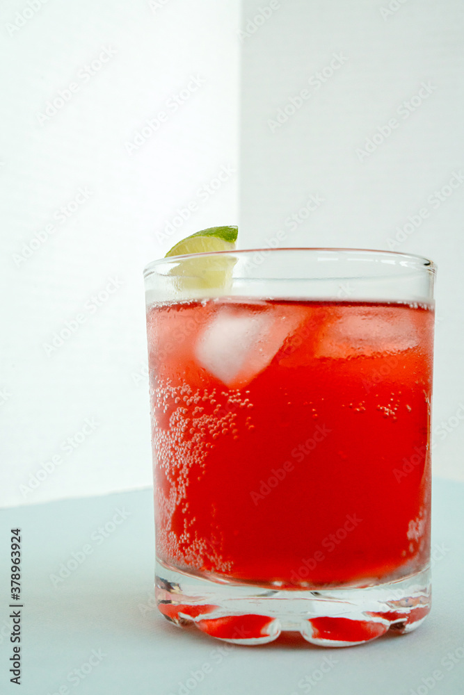 Red sparkling drink in the glass with ice and lime