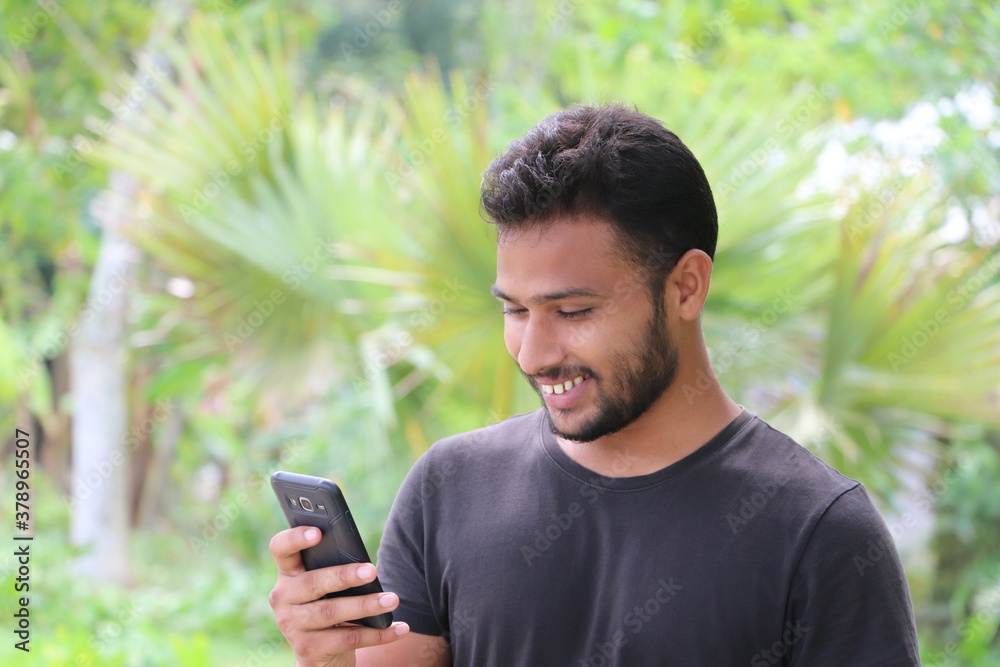 Smiling young man using smartphone, looking at mobile phone screen and enjoying reading messages Smiling young man using smartphone, looking at mobile phone screen and enjoying reading messages