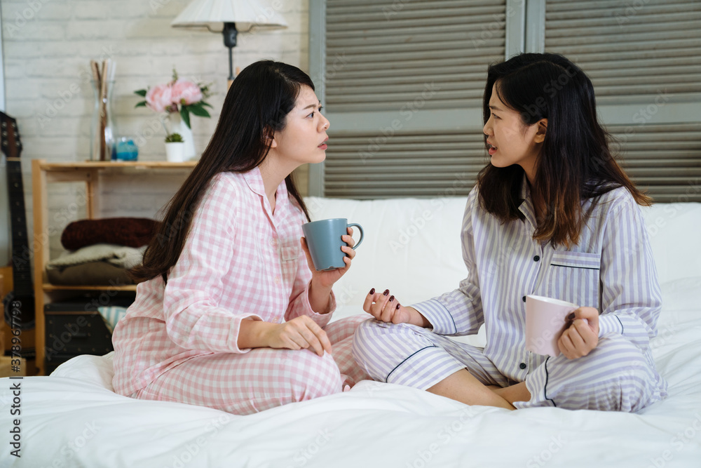 Surprised asian japanese ladies sitting bed and looking at each other with shocked face while listening news chatting gossip. Amazed girls in pajamas sharing problems with cup of coffee in bedroom Surprised asian japanese ladies sitting bed and looking at each other with shocked face while listening news chatting gossip. Amazed girls in pajamas sharing problems with cup of coffee in bedroom