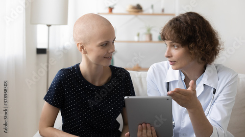 Tableau sur toile Doctor and young hairless sick female cancer patient look at tablet screen discuss treatment or cure together