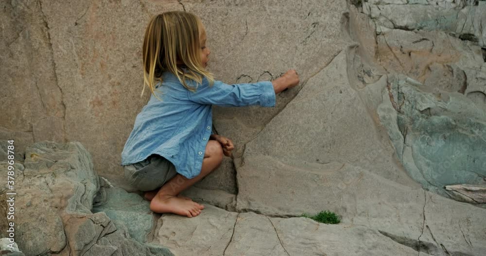 A preschooler is drawing on a rock wall on the beach with charcoal A preschooler is drawing on a rock wall on the beach with charcoal