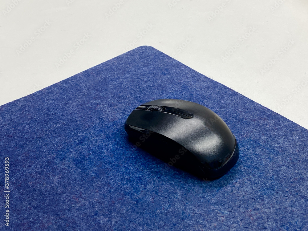 the black wireless mouse on the dark blue mouse pad on the white table the black wireless mouse on the dark blue mouse pad on the white table