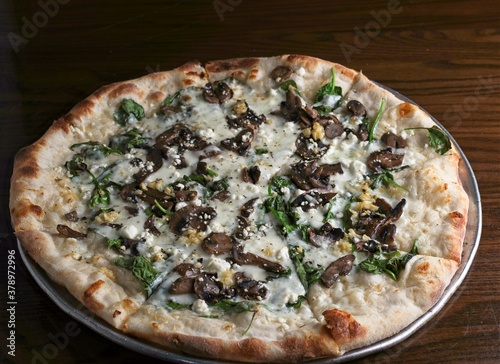 Gourmet pizza white pie with baby spinach, roasted mushroom, fresh garlic & goat cheese.Finished with truffle oil