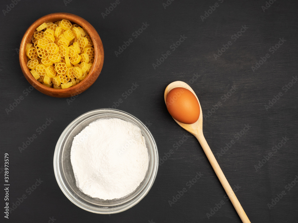 Pasta, flour and egg in spoon on a black wooden background Pasta, flour and egg in spoon on a black wooden background