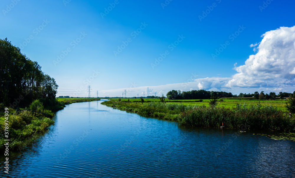 Landscape with river and meadows and power pylons

