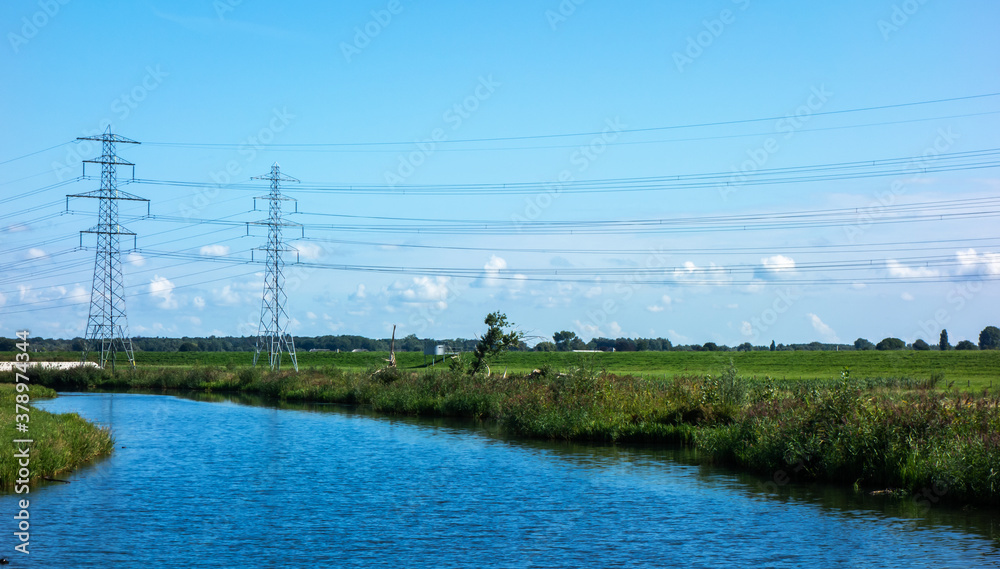 Landscape with river and meadows and power pylons
