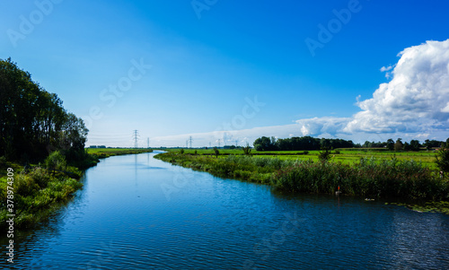 Landscape with river and meadows and power pylons 