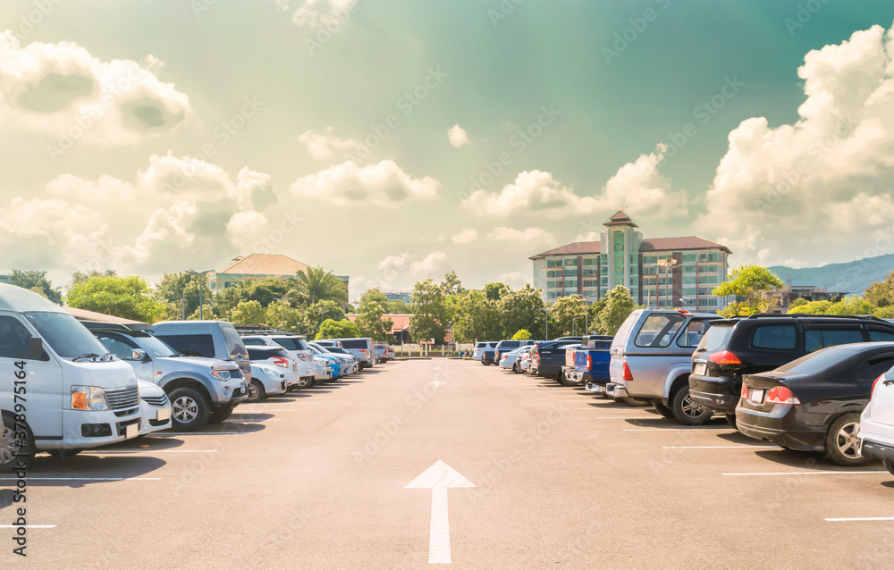 Car parked in large asphalt parking lot in a row with white cloud and blue sky background. Outdoor parking lot with fresh ozone and green environment of travel transportation technology
