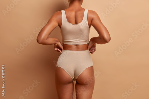 Foto Back view of sensual slim woman poses in panties and top has perfect figure healthy dark skin isolated on brown background