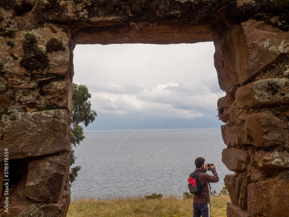Person taking pictures photograph framed in a door or window with a lake and sky landscape behind, in isla del sol, isla de la luna, moon island, sun island, in lake titicaca in bolivia