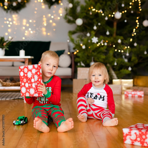 Happy little children in pajamas playing with Christmas presents - beautiful boxes and car. Family Xmas morning in decorated living room with kids gifts and Christmas tree.