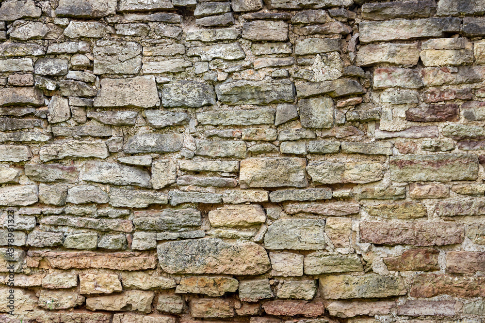 The surface of an old stone wall, masonry of uneven wild hewn stones.