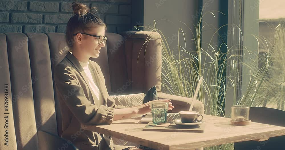 Woman working on notebook, sitting in cafe with coffee cup. Girl in glasses in pause, after work. Online chat with friends, long distance communication. Staying connected. 4K video Slow motion.
