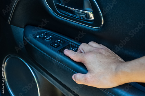 A man's hand is reaching at the car dashboard beside to the car door to press some buttons.