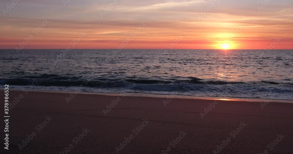 Beautiful golden sunset on empty beach. Pan right along shoreline.