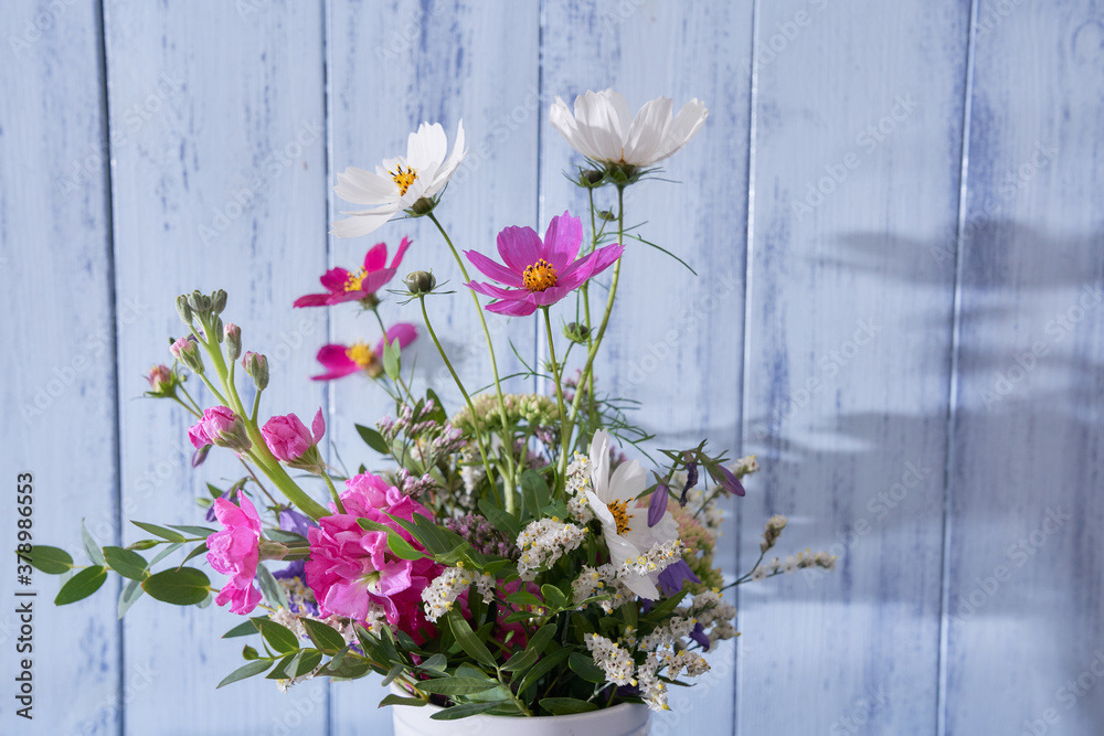 Close-up of multicolored wildflowers standing in a white vase against a blue wall Close-up of multicolored wildflowers standing in a white vase against a blue wall