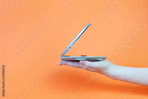 A female hand holds a portable MP-player on an orange background. Copy space - the concept of old technology, music, entertainment, CDs
