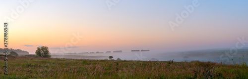 Panoramic view of farm fields and green hills during foggy sunrise