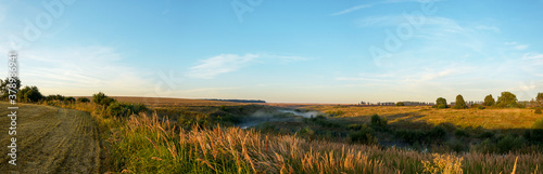 Summer landscape with golden fields and small calm river during sunrise.