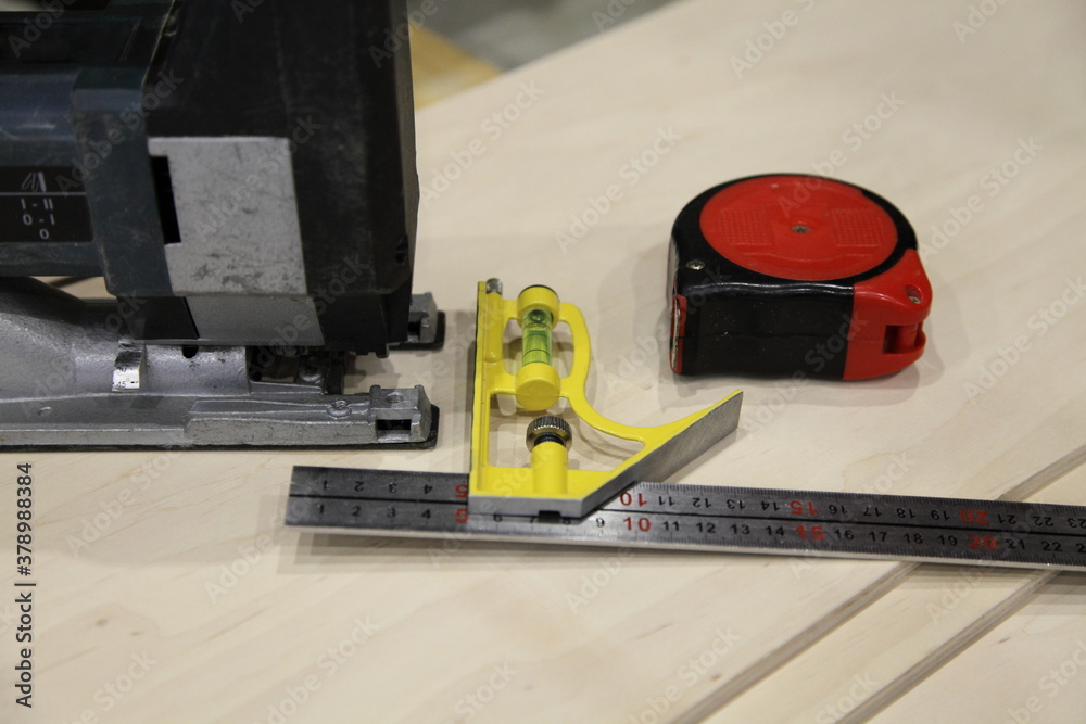 Carpentry marking angle rule, measuring tape and electric jigsaw close-up on plywood sheets background closeup, DIY woodworking instrument Carpentry marking angle rule, measuring tape and electric jigsaw close-up on plywood sheets background closeup, DIY woodworking instrument
