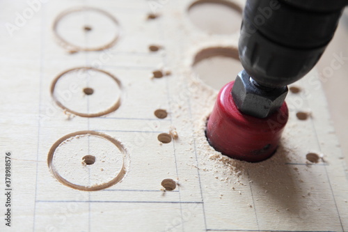 Electric drilling machine with a red circular drill bit crown closeup, DIY drilling of large diameter holes in the plywood