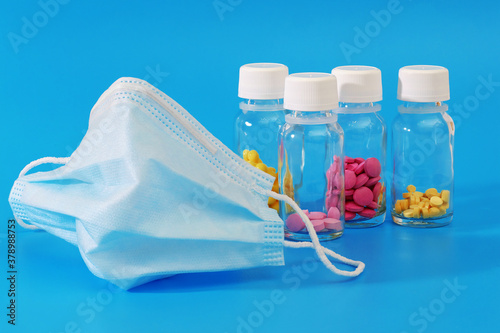 medical face mask and various pills in glass bottles on blue background