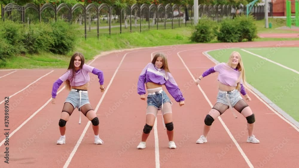 Three young beautiful dancers with long hair in short shorts dancing free style street dancing, hip hop choreography at the stadium. Slow motion Three young beautiful dancers with long hair in short shorts dancing free style street dancing, hip hop choreography at the stadium. Slow motion