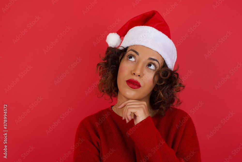 Portrait of thoughtful smiling girl keeps hand under chin, looks sideways, thinking or wondering about something with interest, dressed casually, poses against gray studio. Taking decisions concept. Portrait of thoughtful smiling girl keeps hand under chin, looks sideways, thinking or wondering about something with interest, dressed casually, poses against gray studio. Taking decisions concept.