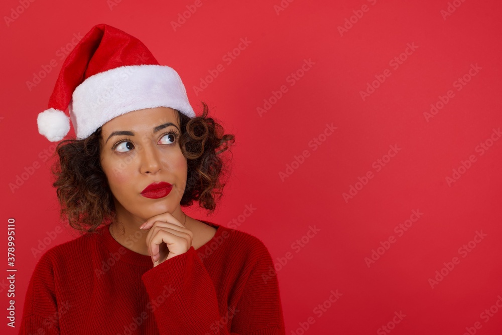 Portrait of thoughtful woman keeps hand under chin, looks away trying to remember something or listens something with interest, dressed casually, poses indoors. Youth concept. Portrait of thoughtful woman keeps hand under chin, looks away trying to remember something or listens something with interest, dressed casually, poses indoors. Youth concept.