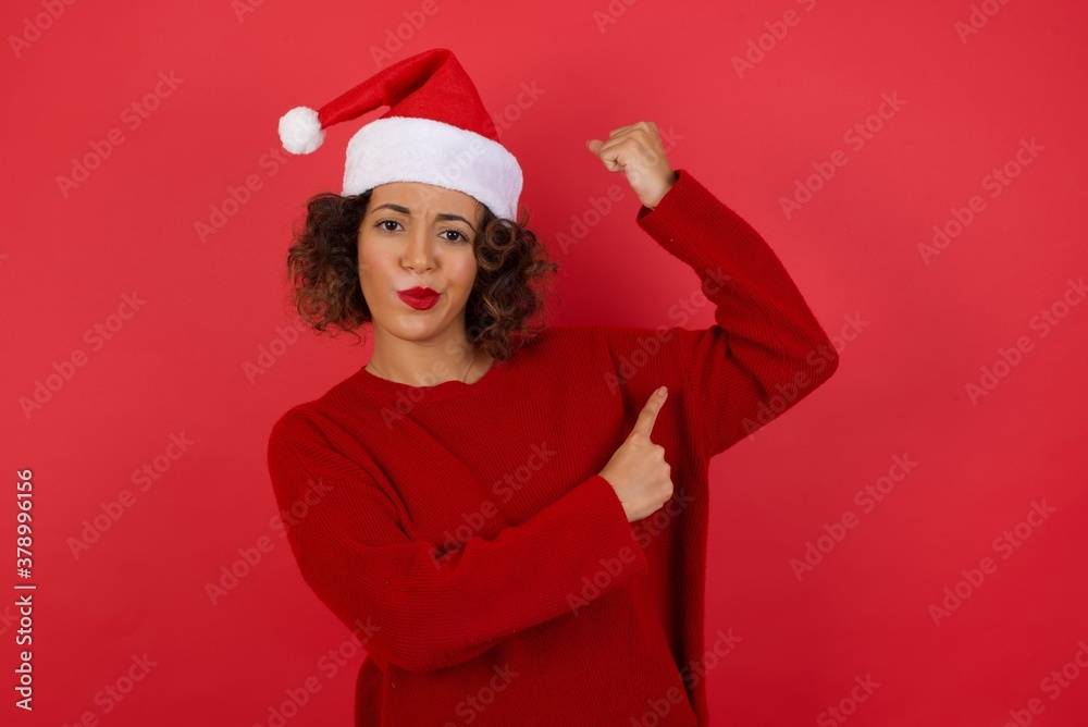 Waist up shot of blonde woman raises hand to show her muscles, feels confident in victory, looks strong and independent, smiles positively at camera, stands against gray background. Sport concept. Waist up shot of blonde woman raises hand to show her muscles, feels confident in victory, looks strong and independent, smiles positively at camera, stands against gray background. Sport concept.
