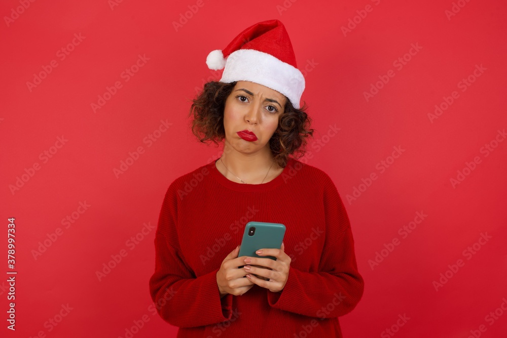 Portrait of a confused Caucasian woman holding mobile phone and shrugging shoulders and frowning face over isolated over gray background Portrait of a confused Caucasian woman holding mobile phone and shrugging shoulders and frowning face over isolated over gray background