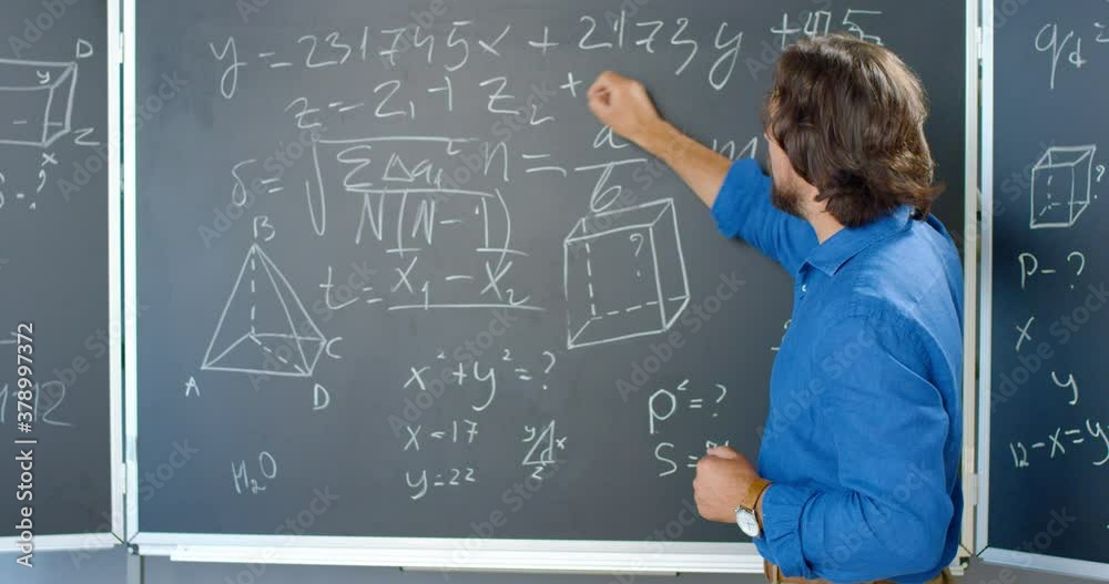 Caucasian male teacher standing at blackboard with formulas, graphics and laws and explaining math. Man writing on board with chalk. Lecturer of mathematics at school or college. Caucasian male teacher standing at blackboard with formulas, graphics and laws and explaining math. Man writing on board with chalk. Lecturer of mathematics at school or college.