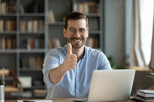 Foto Portrait of smiling young Caucasian man in glasses sit at desk work on laptop recommend online course or training