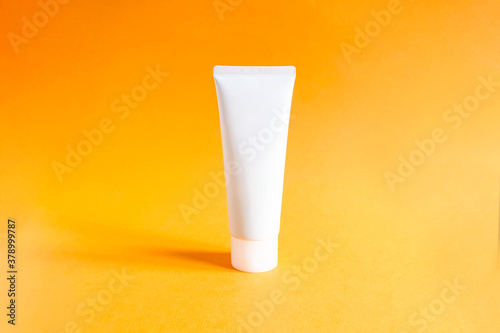 Mock-up of unbranded white bottle for branding and label on a textured bright orange background. Squeeze bottle plastic tube. Natural organic spa cosmetics concept.