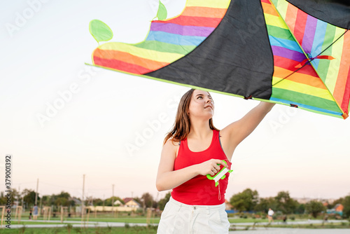 Young woman flying a kite in a public park at sunset